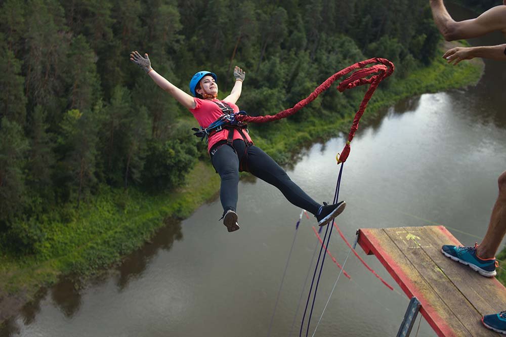 Woman bungee jumping over a river surrounded by lush forest