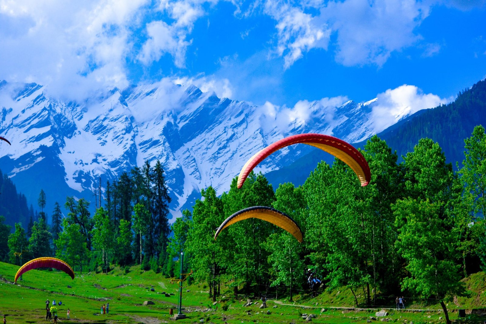 Paragliding over lush green landscape of manali with snow-capped mountains in the background