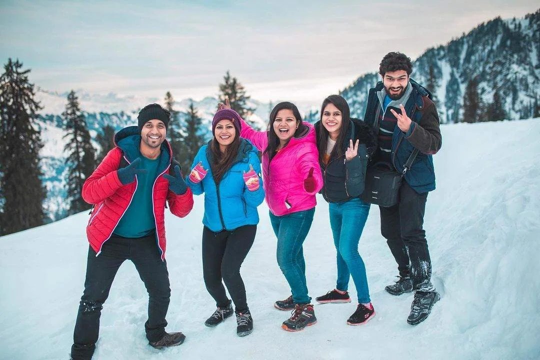 Group of male friends in colorful winter jackets smiling while capturing memories of the snowy mountain of Manali