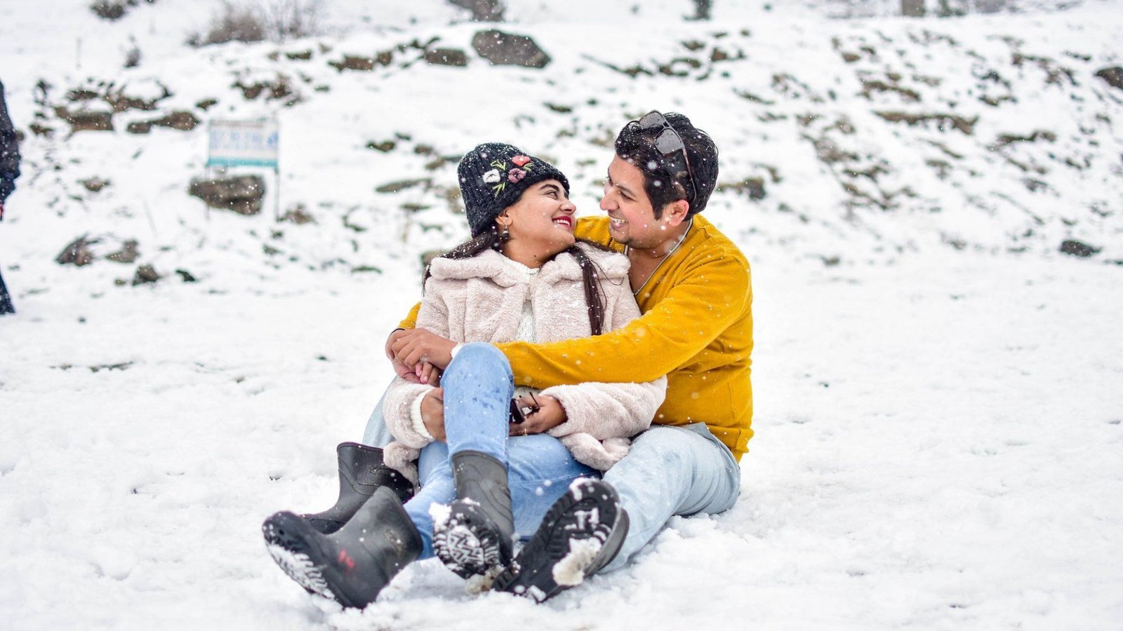 Couple smiling and embracing while sitting in snow 