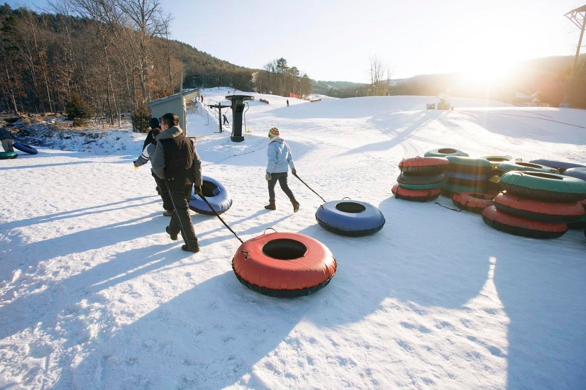People snow tubing down a snowy hill, pulling inner tubes.